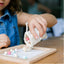 Girl pouring wooden beads out of calico bag onto wooden beading board