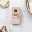 Box of a rose gold safety razor on a marble surface with a bar of soap and towel.