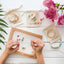 Poppy and daisy designs friendship necklace kit contents laid out showing child's hands placing bead onto thread