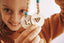 Girl smiling in background holding up two completed Kids making poppy and daisy pastel bag tags