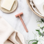 Rose gold safety razor on a marble surface with a bar of soap, towel, and flowers.