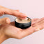 Woohoo armpit detox mask tin open on ladies hand dipping finger into mask to show consistency of product