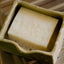 Bar of dishwashing soap with suds in a green ceramic dish on a wooden surface