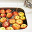 Apples being washed in produce wash in a sink with water flowing from a faucet.