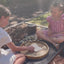 Two girls playing tic tac toe outside on park bench